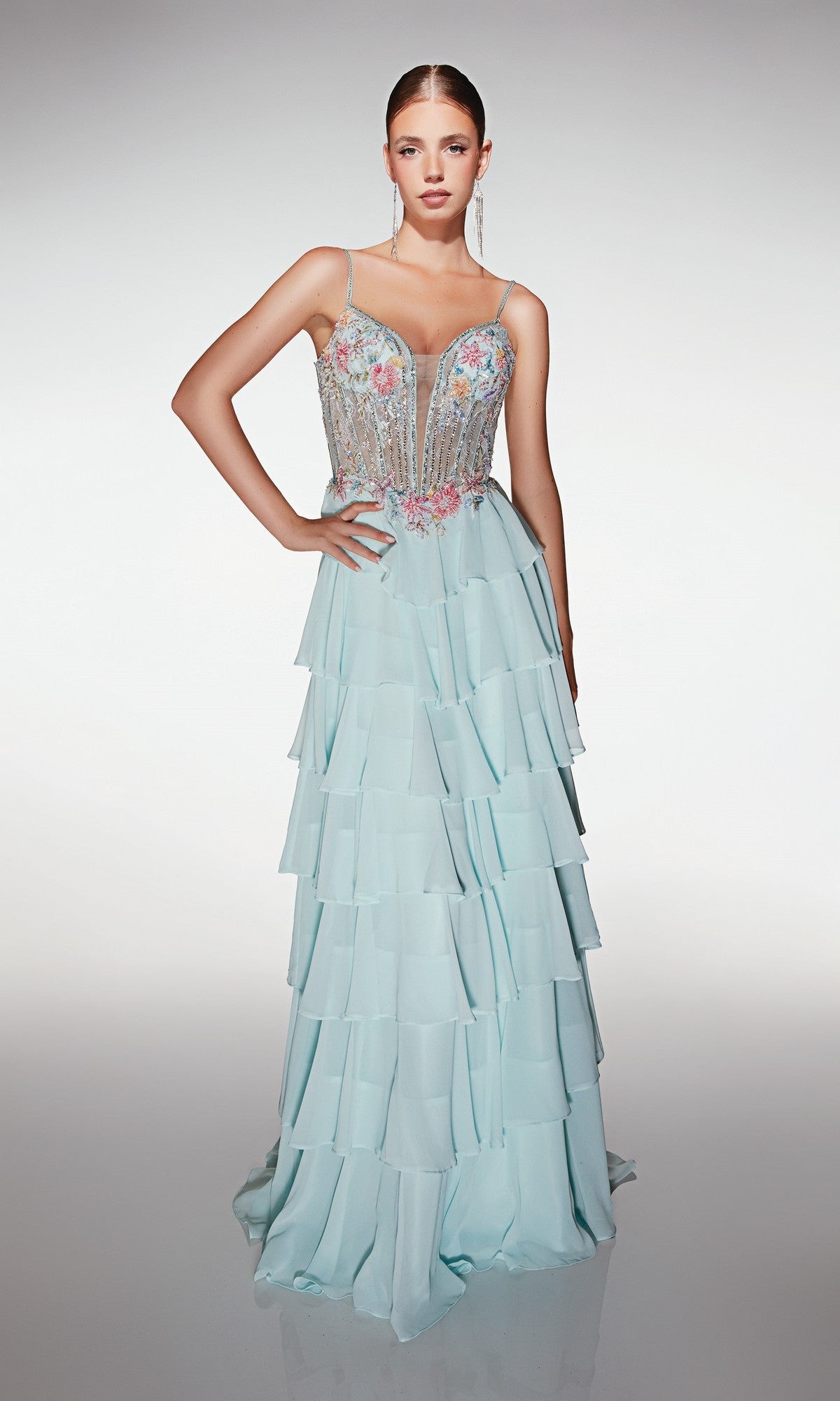 A woman wears the Long Prom Dress Alyce 61993, featuring a floral corset bodice with thin straps, long earrings, and a light blue chiffon tiered ruffle skirt.